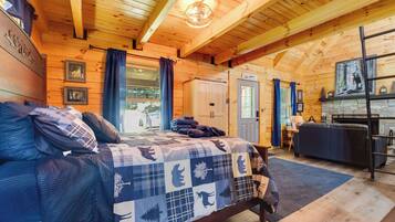 Interior de una cabaña de madera con cama, chimenea y comedor.