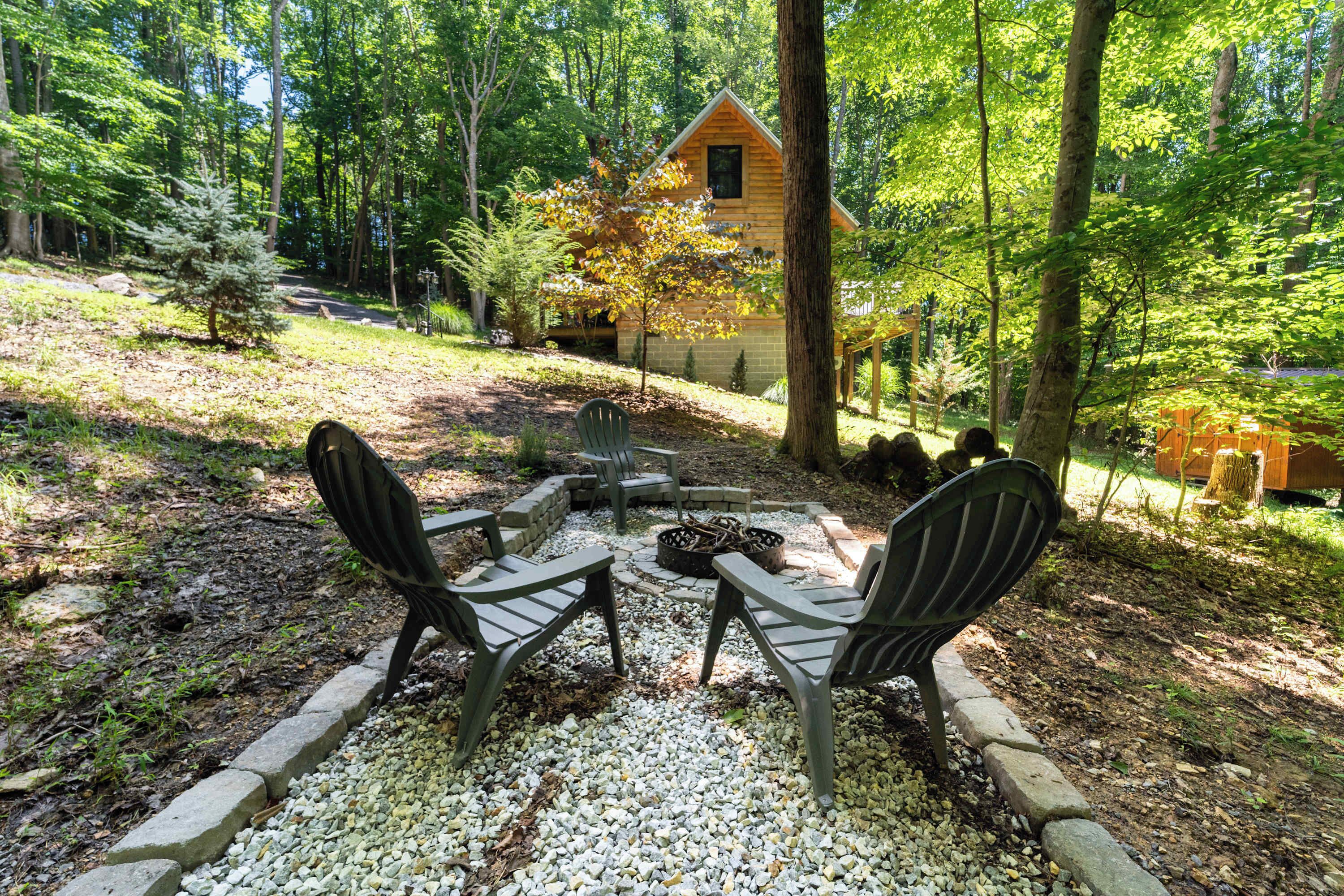 A cabin with a fire pit and chairs in a forest setting.
