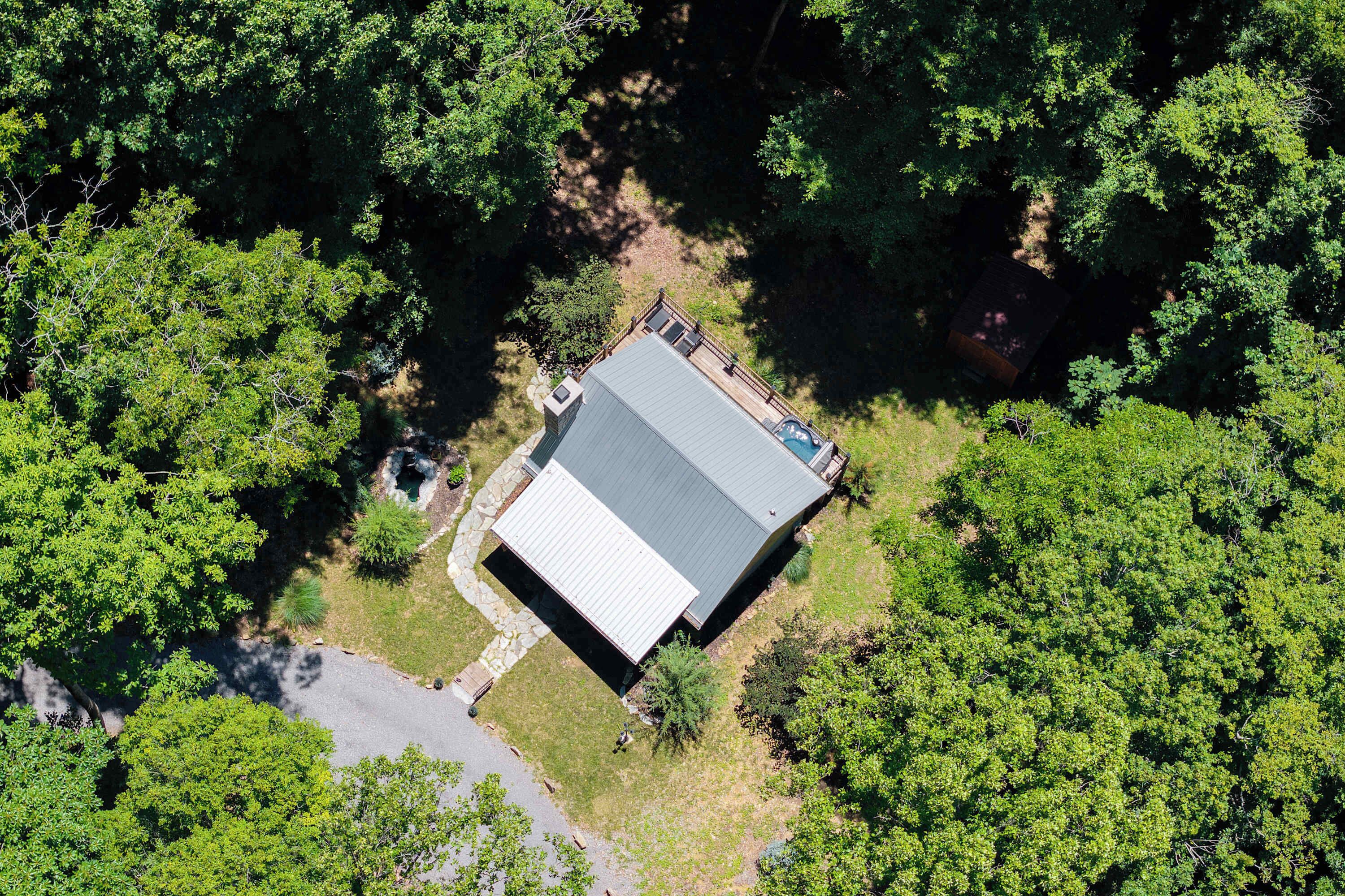 An aerial view of a property surrounded by dense forest, featuring a large building with a flat roof and a swimming pool.