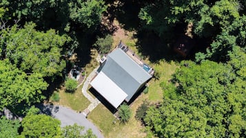 An aerial view of a property surrounded by dense forest, featuring a large building with a flat roof and a swimming pool.