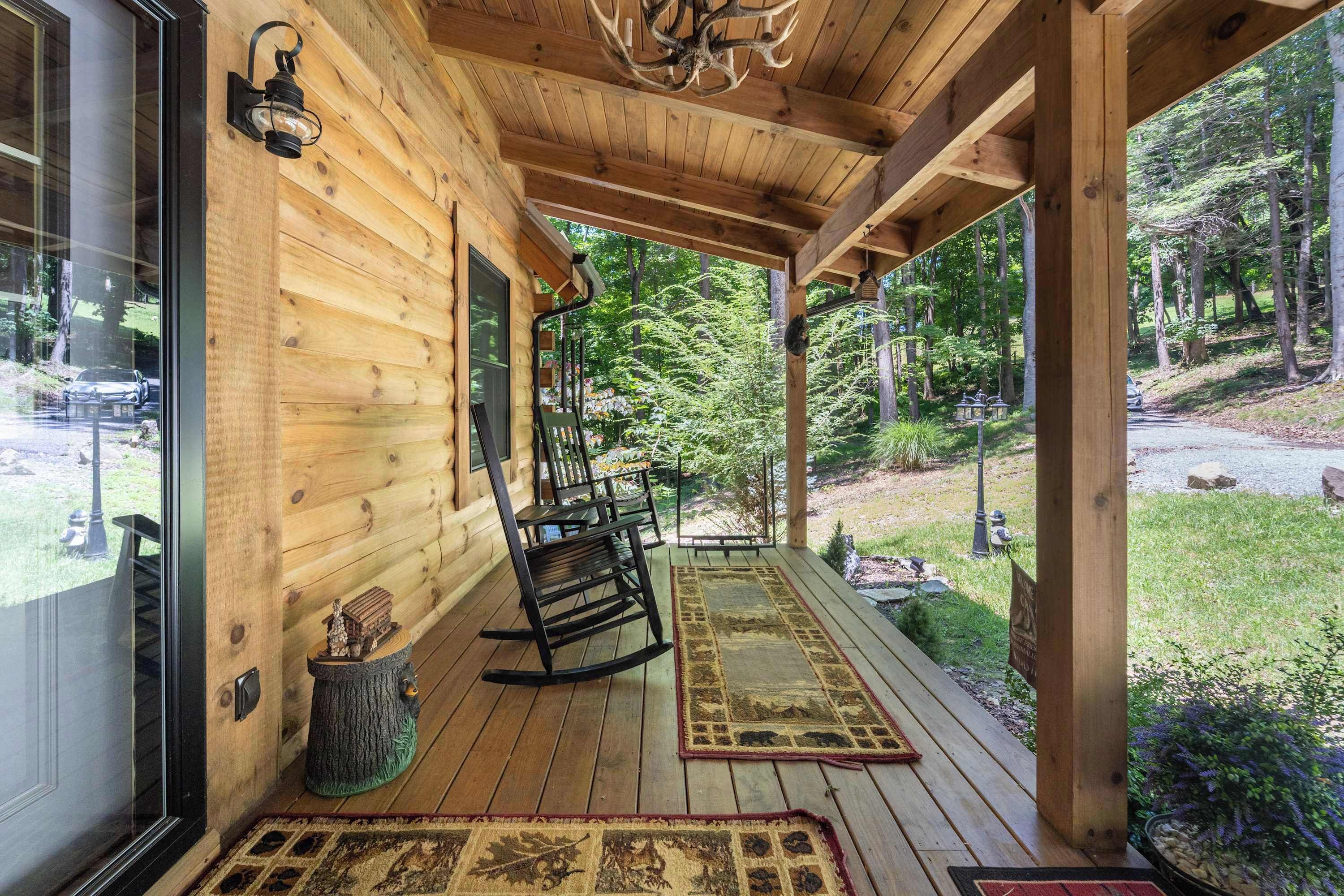 Una cabaña de madera con un porche, mecedoras y vistas al bosque circundante.