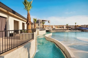 Ein Schwimmbecken mit geschwungenem Design, Palmen und ein Gebäude mit Balkon.