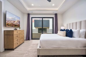 Ein Schlafzimmer mit einem Bett, einem Schminktisch, einem Fernseher und einem Balkon mit Vorhängen.