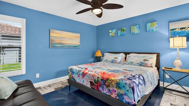 A bedroom with a bed, a ceiling fan, a window with blinds, and artwork on the walls. - Private Pool + Spa + Outdoor Dining | Gulf Beaches | Blue Sunset (Bonita Springs)