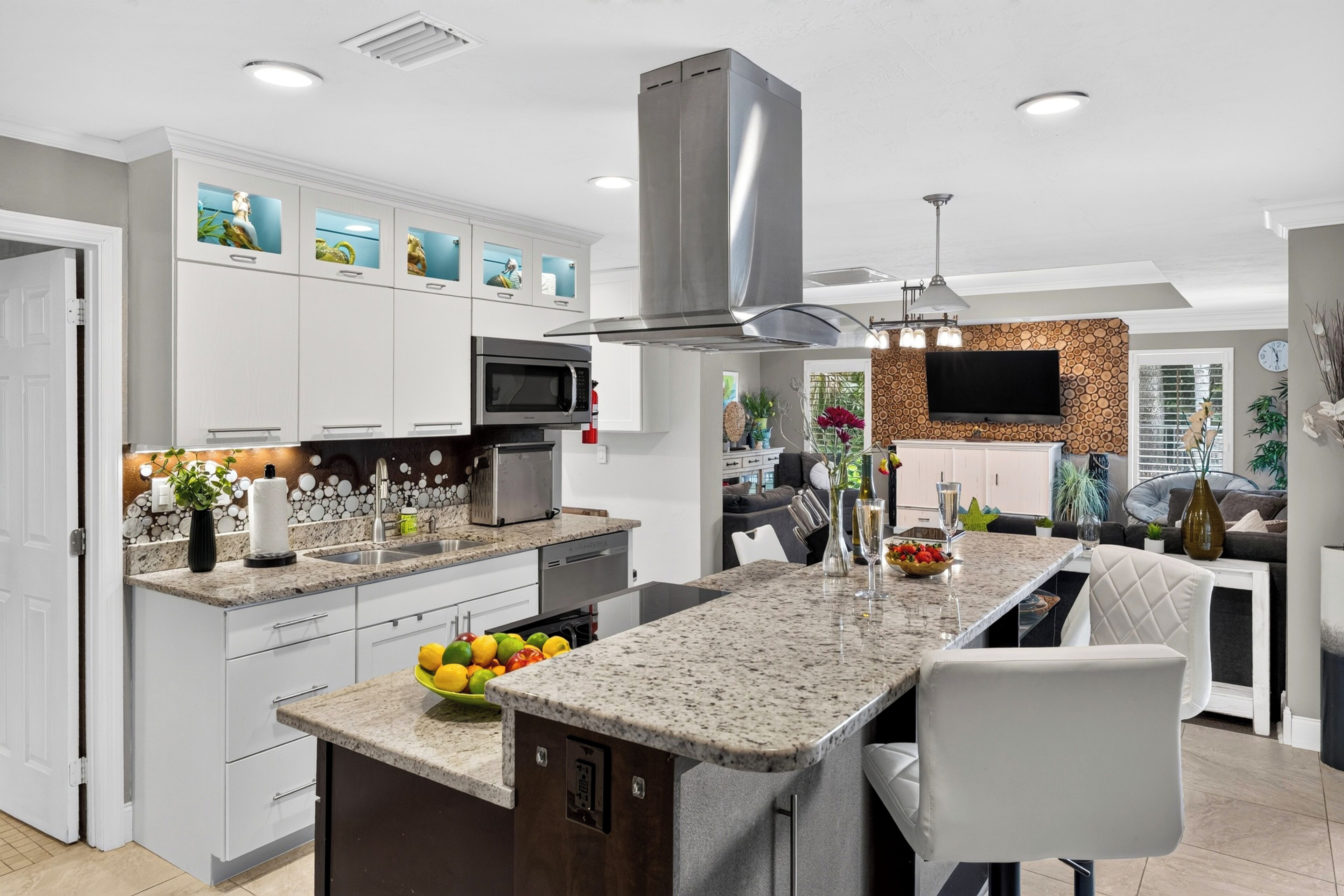 A modern kitchen with white cabinets, a granite countertop, a stainless steel range hood, and a built-in microwave.