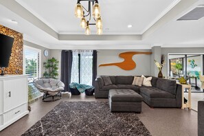 Una sala de estar moderna con un sofá modular, una lámpara colgante y una gran obra de arte abstracto en la pared.