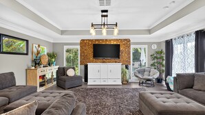 A modern living room with a flat-screen TV, grey sofas, a patterned rug, and a white cabinet. - Private Pool + Spa + Outdoor Dining | Gulf Beaches | Blue Sunset (Bonita Springs)