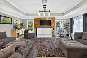 A modern living room with a flat-screen TV, grey sofas, a patterned rug, and a white cabinet. - Private Pool + Spa + Outdoor Dining | Gulf Beaches | Blue Sunset (Bonita Springs)