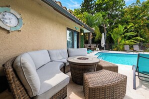 A poolside area with a wicker sofa, a round table, and a clock on the wall. - Private Pool + Spa + Outdoor Dining | Gulf Beaches | Blue Sunset (Bonita Springs)