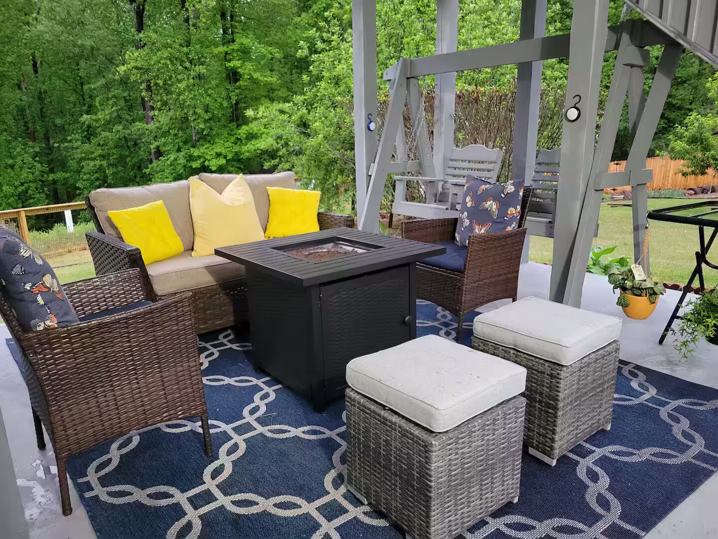 An outdoor patio with wicker furniture, a black table, and a blue patterned rug.