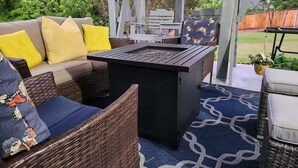 En udendørs patio med fletmøbler, et sort bord og en blå tapetgrå måtte.