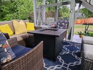 Eine Terrasse im Freien mit Korbmöbeln, einem schwarzen Tisch und einer blauen Teppich.