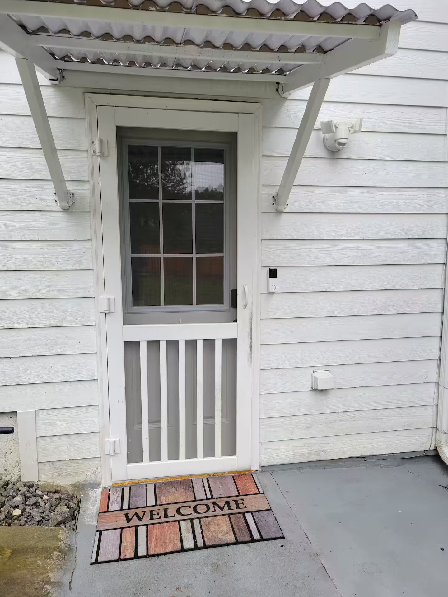 A white wooden house with a front door, a window, and a welcome mat.