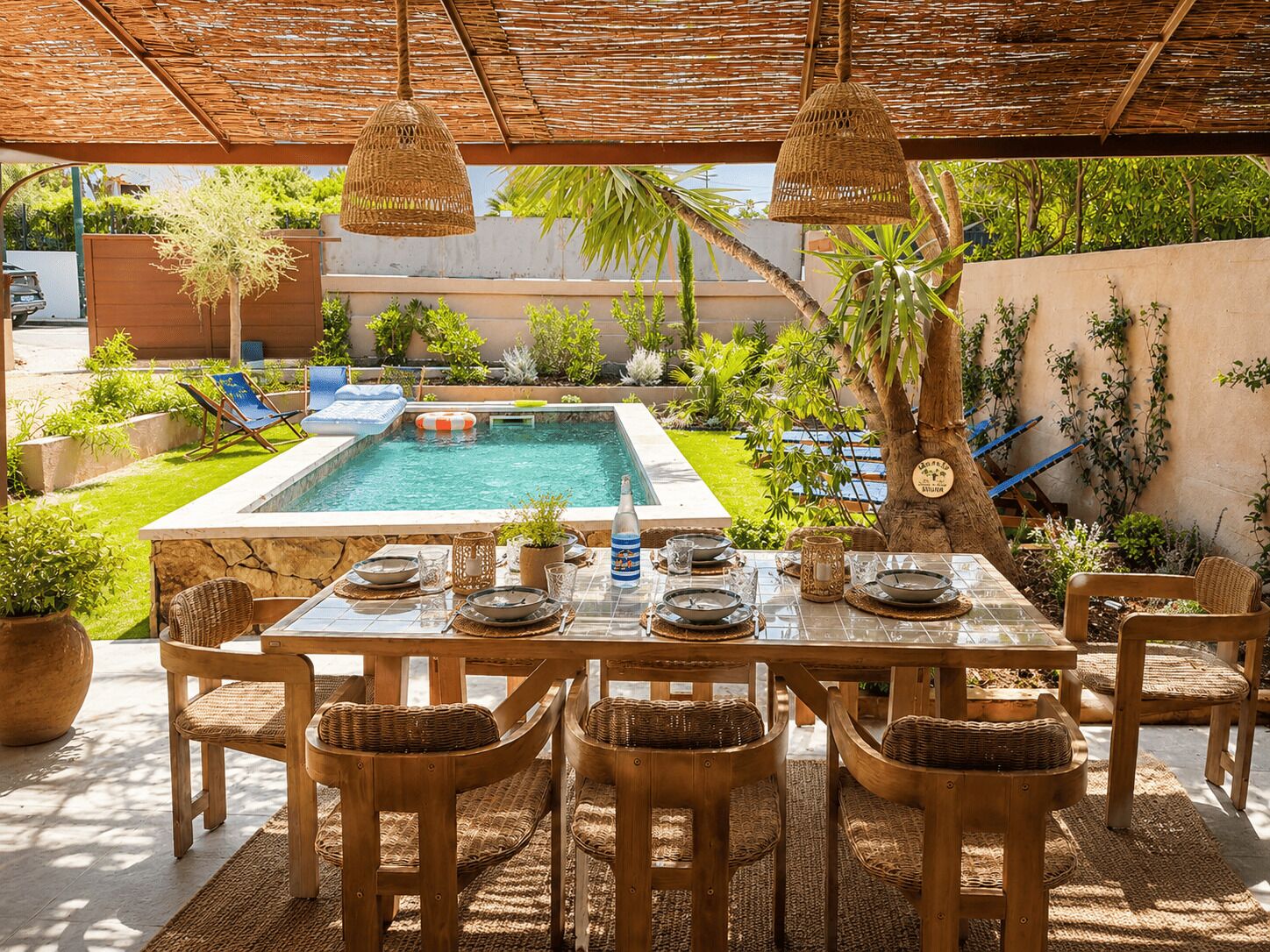 Un espacio exterior para comer con piscina, mobiliario de mimbre y una zona de estar cubierta.