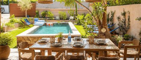 An outdoor dining area with a pool, wicker furniture, and a covered seating area.