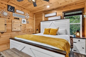 A cozy wooden room with a bed, a nightstand, and a window with a view of greenery. - Sleeps 27 • Pool + Hot Tub + Theater + Near Pigeon Forge | It’s Got It All Y’all (Pigeon Forge)