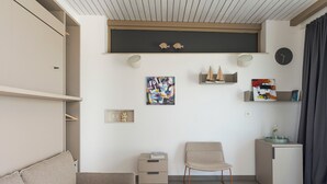 A modern living room with a sofa, a chair, a small cabinet, and a shelf with decorative items. - Splendid sea-view villa in Marzamemi, Di Casa In Sicilia (Noto)