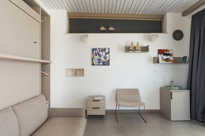 Ein modernes Wohnzimmer mit einer Couch, einem Sessel, einer kleinen Kommode und einem Regal mit Dekoration.