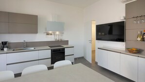A modern kitchen with a built-in oven, a sink, and a dining area with a table and chairs. - Splendid sea-view villa in Marzamemi, Di Casa In Sicilia (Noto)