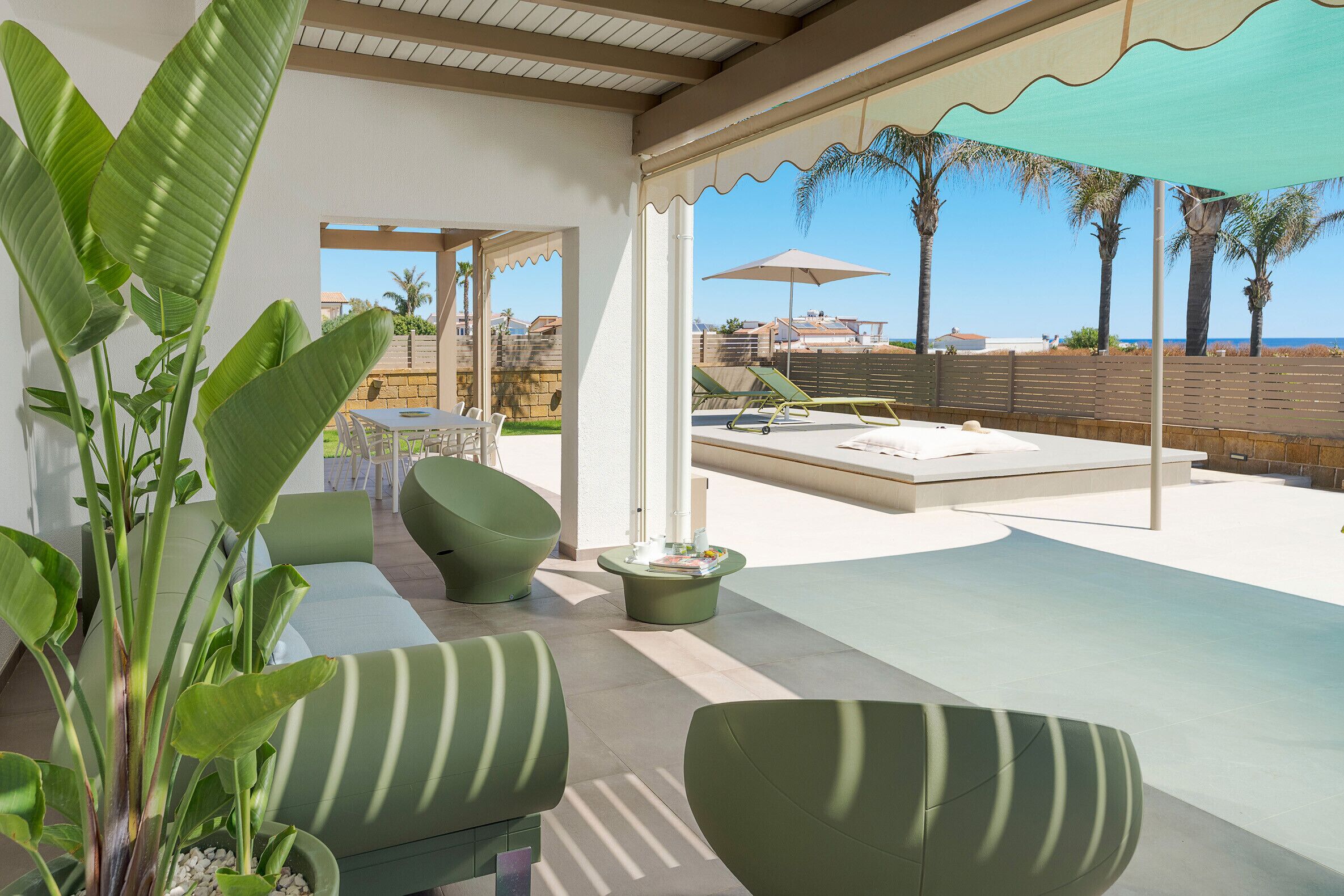 A covered outdoor seating area with a pool, lounge chairs, and a view of the sea.
