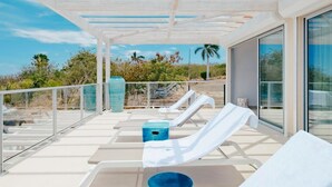 Eine Sonnenterrasse mit Liegestühlen und einer blauen Schale, mit Blick auf eine Landschaft mit Palmen.