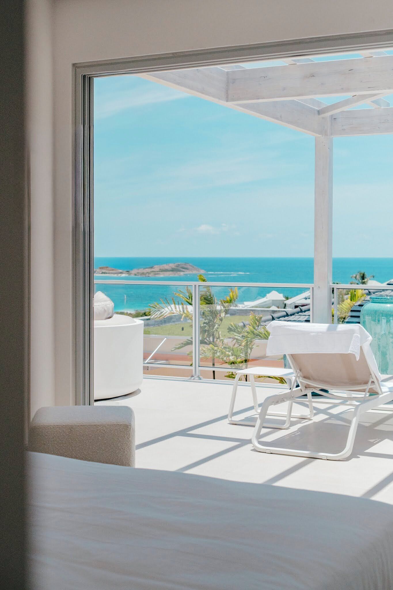 A balcony with a view of the ocean, a white chair, and a white sofa.