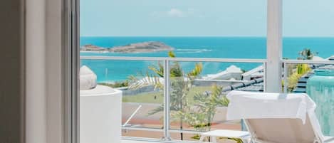 Un balcón con vista al océano, una silla blanca y un sofá blanco.