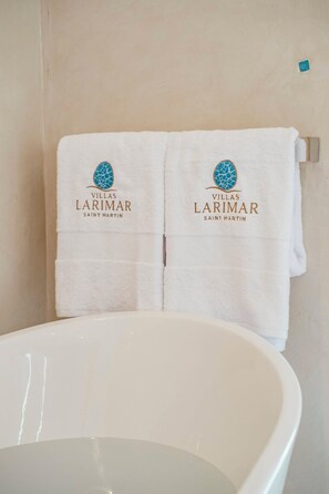 Et badeværelse med et hvidt badekar og to håndklæder hængende på en håndklædestang, hvorpå der ses logo og navn 'Villas Larimar Saint Martin'.