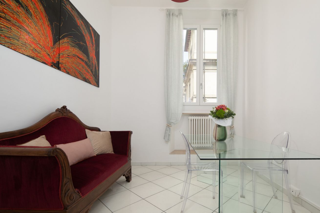 A room with a red sofa, a glass table, and a window with white curtains.
