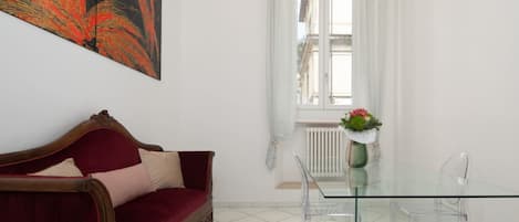A room with a red sofa, a glass table, and a window with white curtains.
