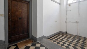 Um corredor com piso xadrez, uma porta de madeira e uma parede branca com uma janela.