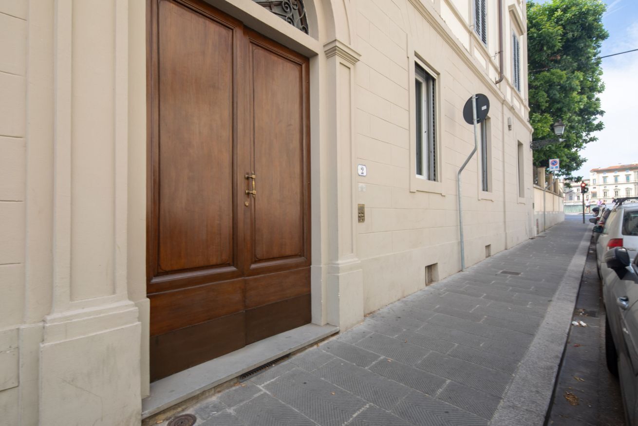 A building with a large wooden double door, a narrow sidewalk, and a parked car on the right.