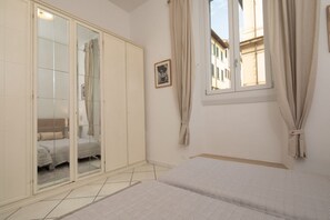 Ein Schlafzimmer mit Bett, Kleiderschrank, einem Fenster mit Vorhängen und Blick auf Gebäude.