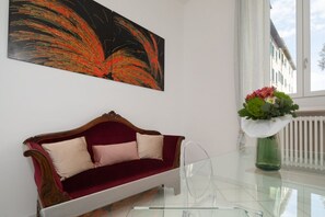 A room with a red velvet sofa, a clear glass table, a green vase with flowers, and a large abstract painting on the wall. - Experience the authentic charm of Florence in this elegant apartment located on Via Sant'Onofrio, in the historic Oltrarno district—one of the city's most charming, authentic, and sought-after neighborhoods.Blending contemporary design with carefully s (Firenze)
