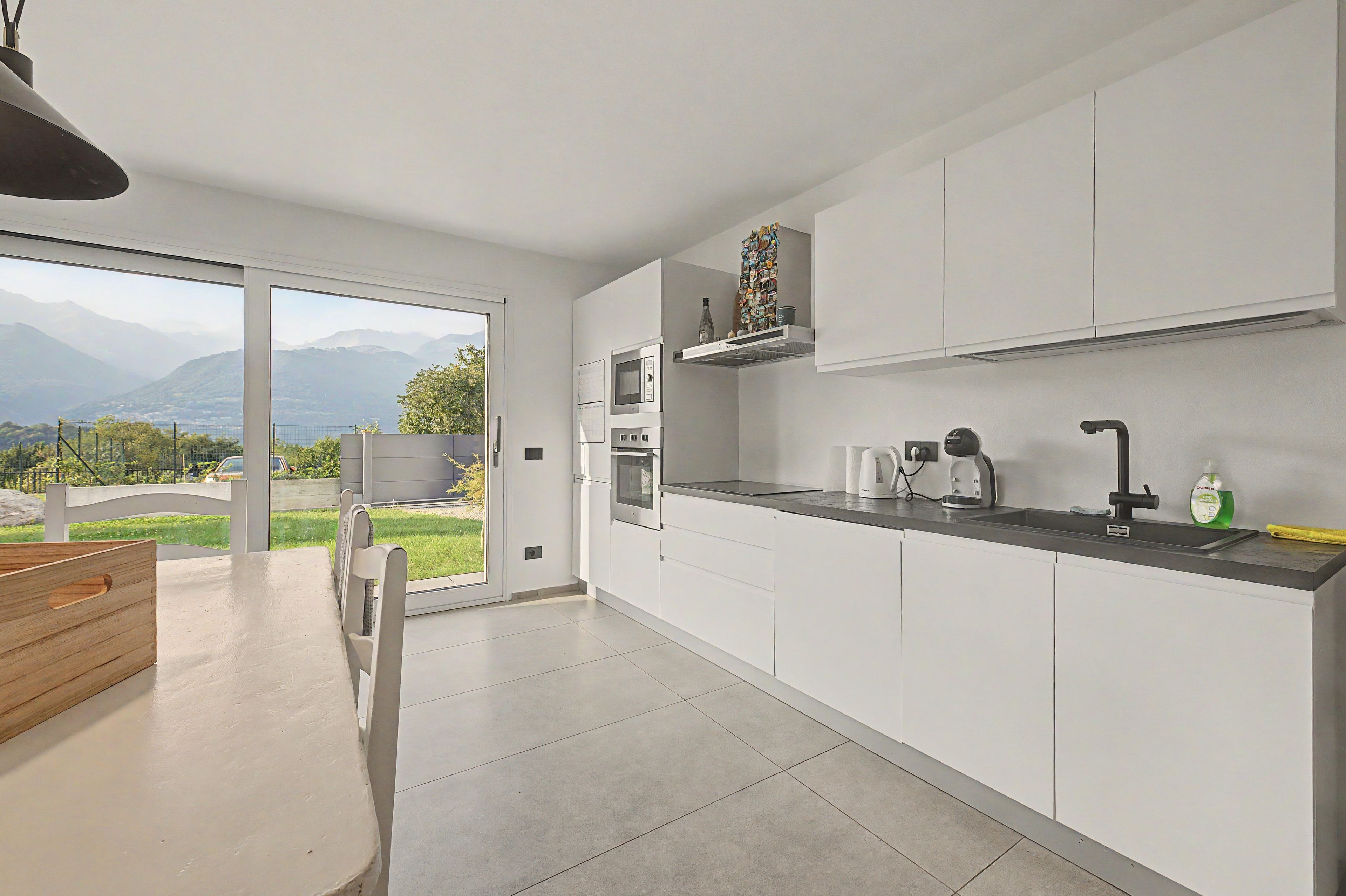 Cocina moderna con armarios blancos, microondas integrado y vistas a montañas a través de amplios ventanales.