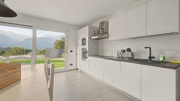 Cocina moderna con armarios blancos, microondas integrado y vistas a montañas a través de amplios ventanales.