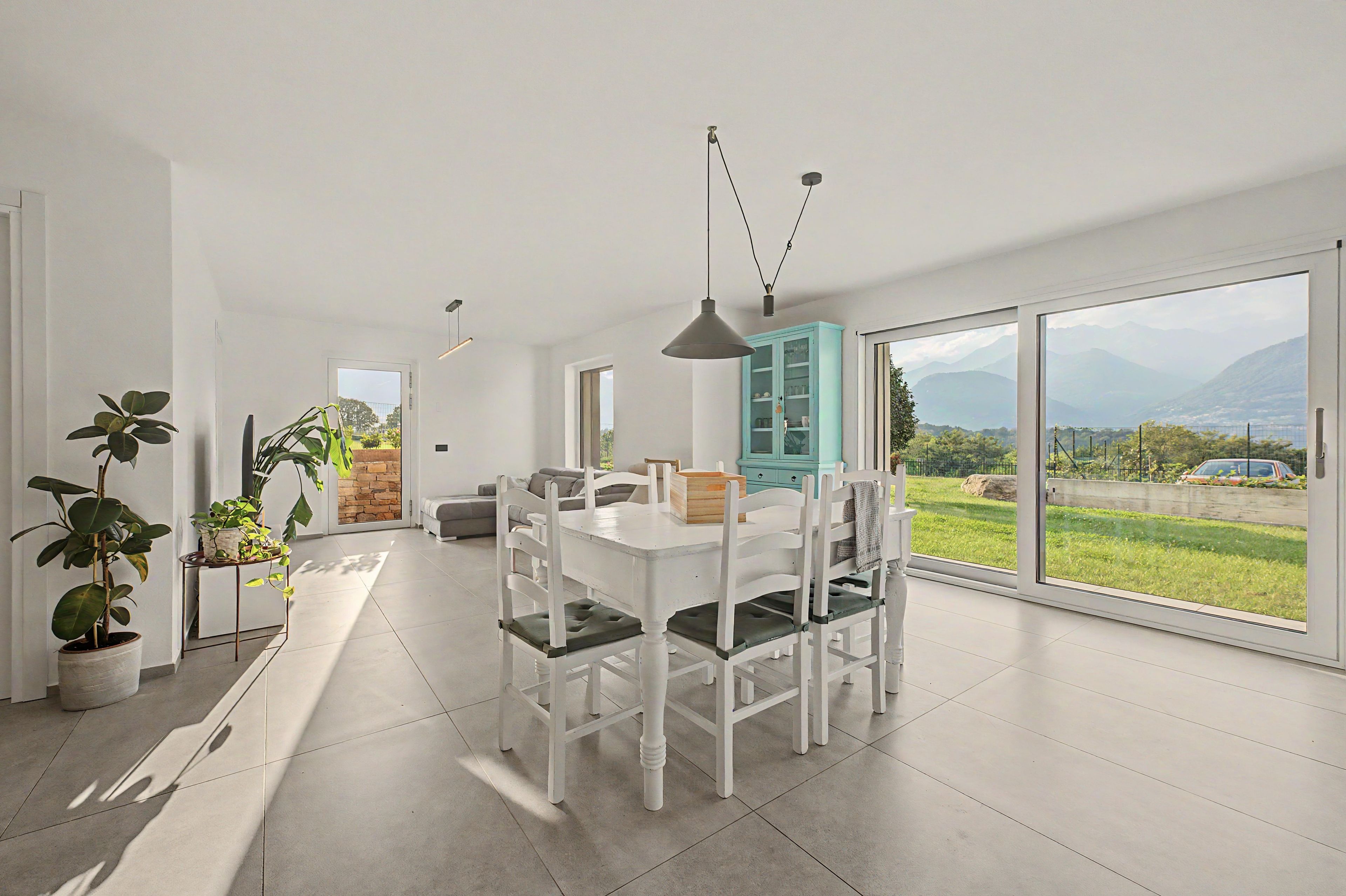 Ein moderner Essbereich mit einem weißen Tisch und Stühlen, einem blauen Schrank und Blick ins Freie.