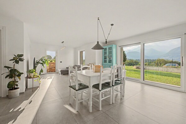 A modern dining area with a white table and chairs, a blue cabinet, and a view of the outdoors.