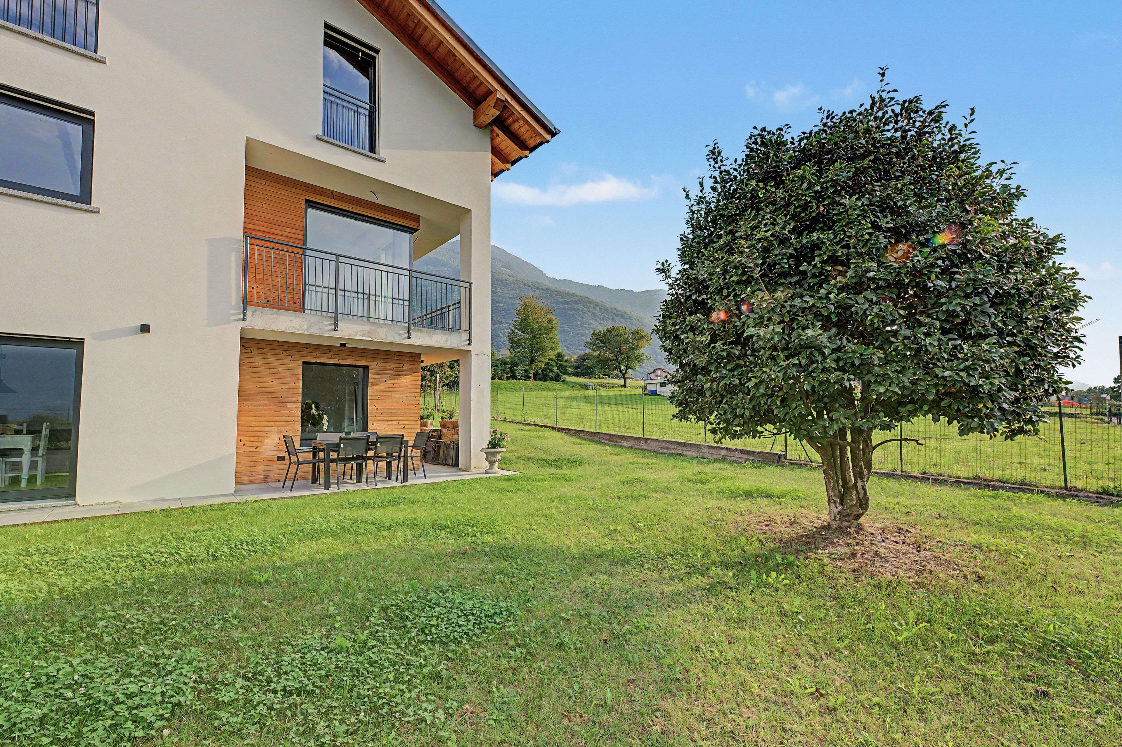 A two-story building with a balcony, a dining area with outdoor furniture, and a well-maintained lawn.