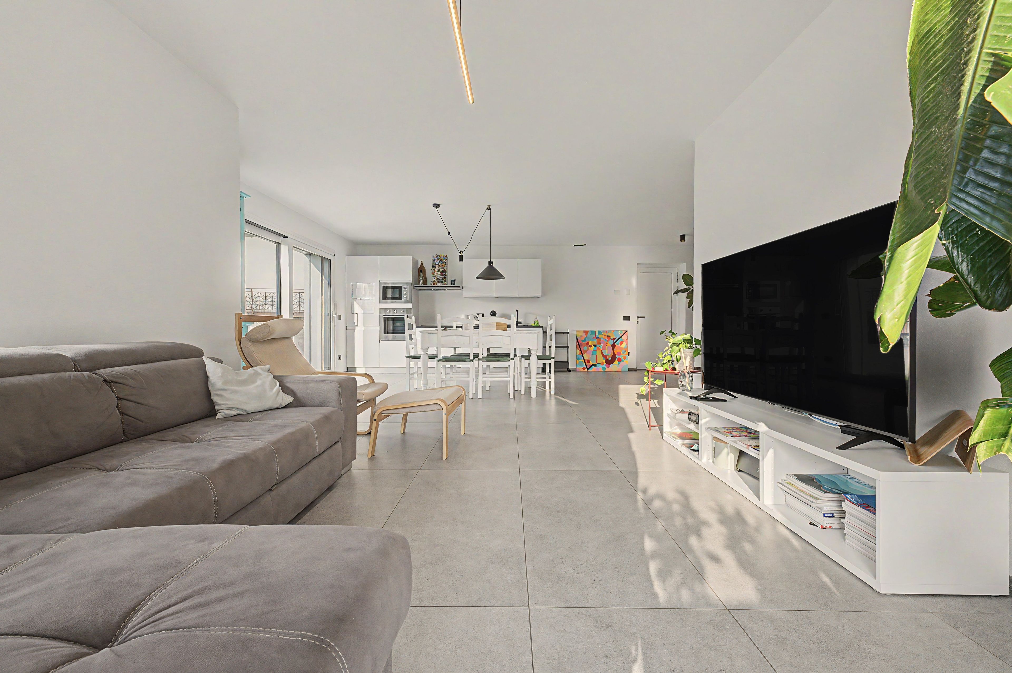Una sala de estar moderna con un sofá, un televisor y un comedor con sillas y una mesa.