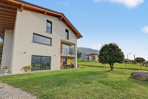 A modern two-story house with a balcony, large windows, and a well-maintained lawn.