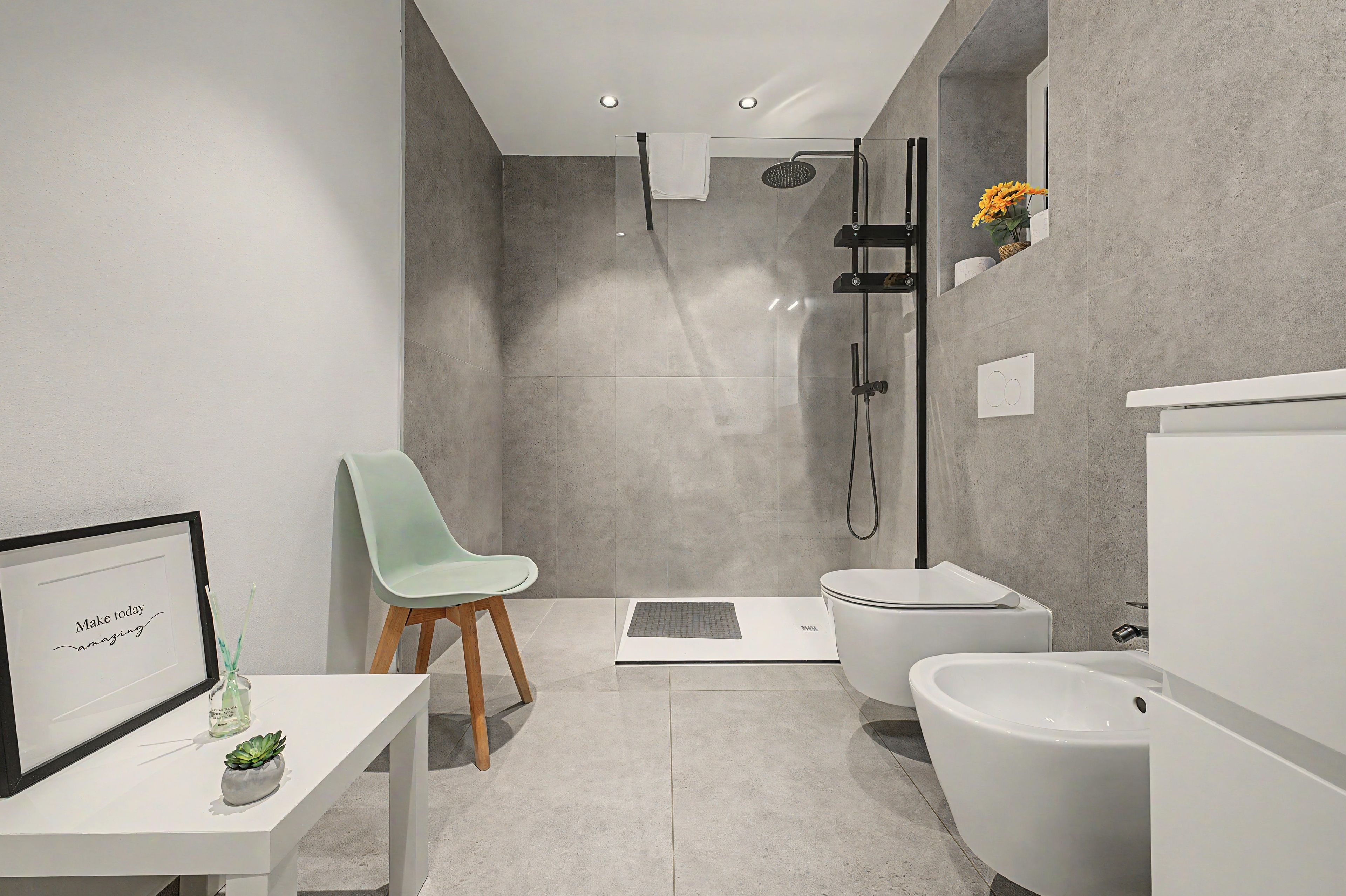 Ein modernes Badezimmer mit Dusche, Toilette, Bidet und einem kleinen Tisch mit Stuhl und einem gerahmten Bild.