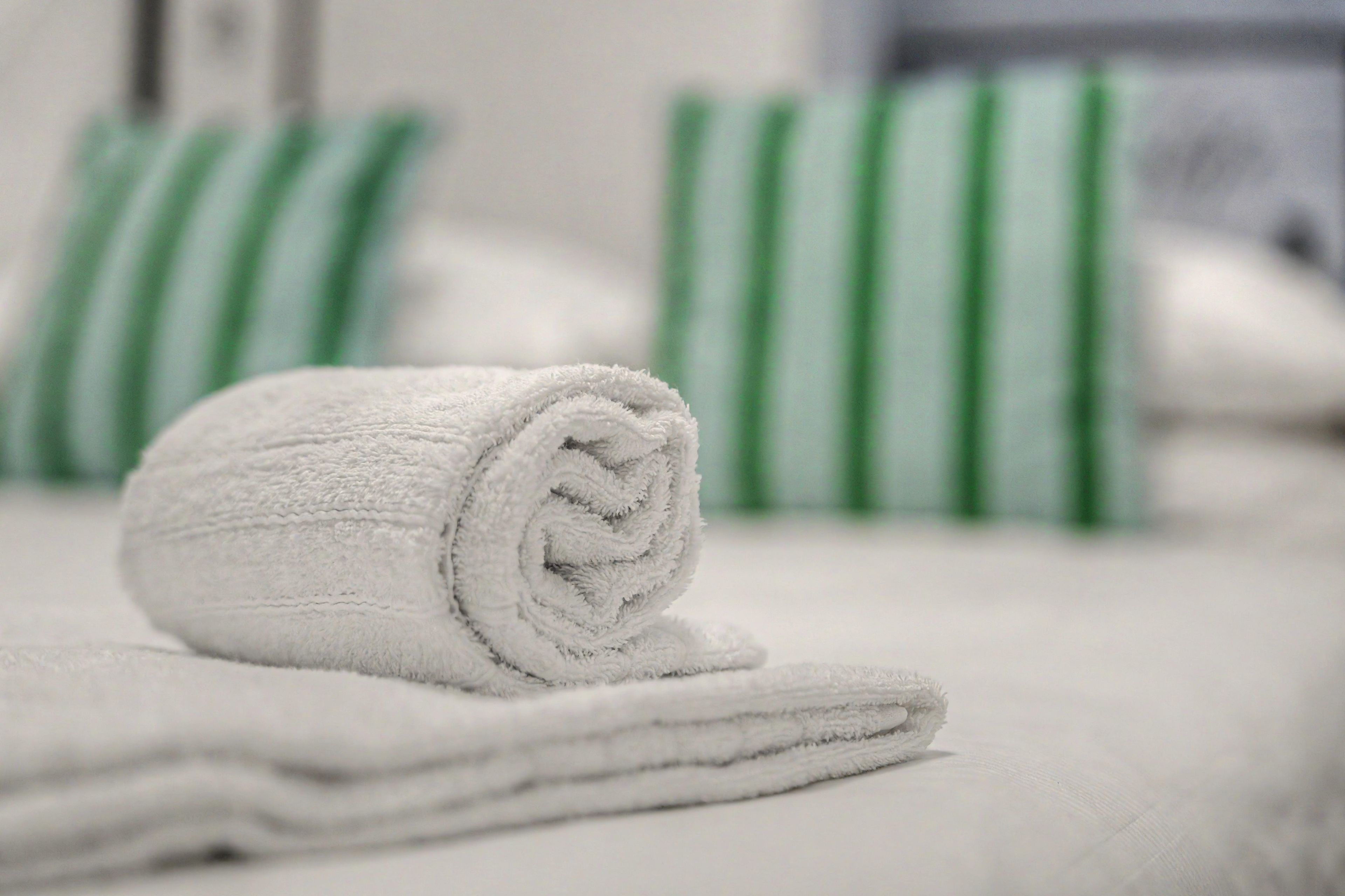 Una toalla blanca doblada ordenadamente sobre una cama con almohadas a rayas verdes.