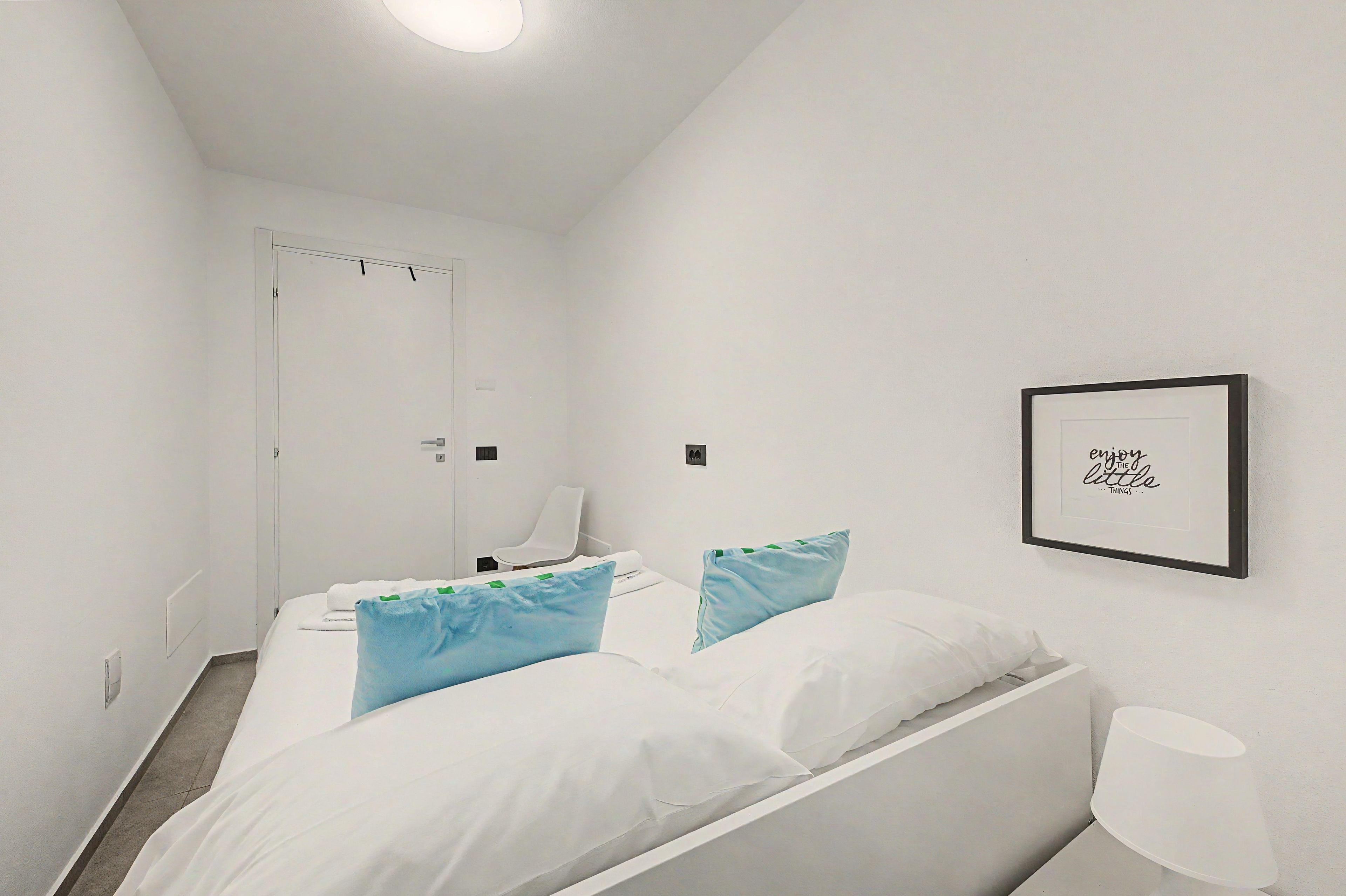 Une chambre d’hôtel comprenant un lit, deux oreillers, une chaise, une table de chevet et un tableau accroché au mur.