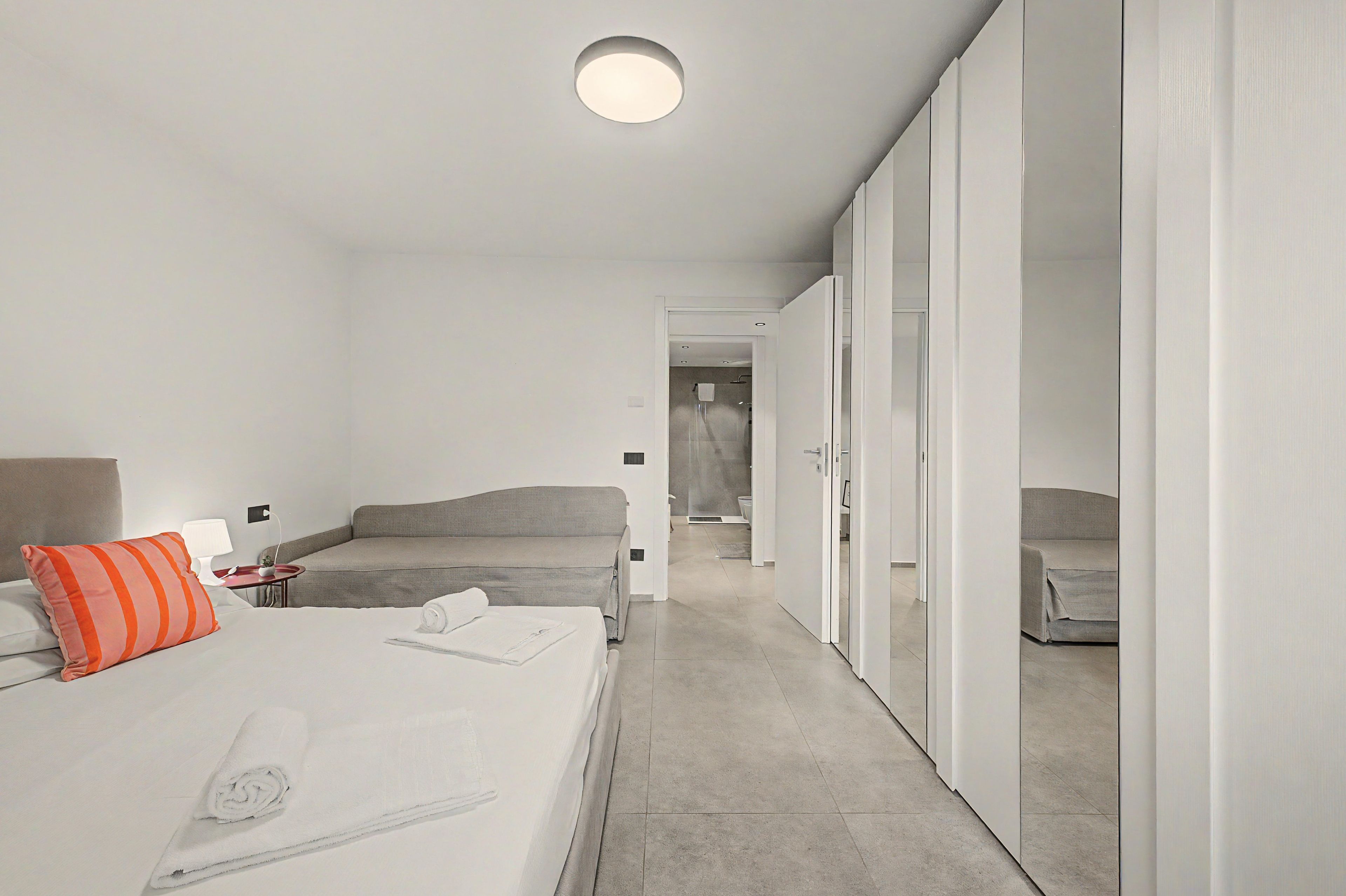 Una habitación de hotel moderna con una cama, una mesita de noche, una lámpara y un armario.