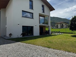 A modern two-story house with a covered patio, a gravel driveway, and a well-maintained lawn. - Apartment 'Tommaso' in Villa Flaminia, Colico, with Garden and BBQ (Colico)