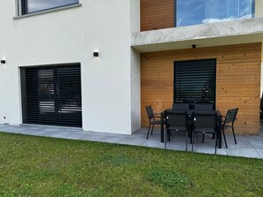 An outdoor seating area with a table and chairs, a wooden wall, and a window with blinds. - Apartment 'Tommaso' in Villa Flaminia, Colico, with Garden and BBQ (Colico)