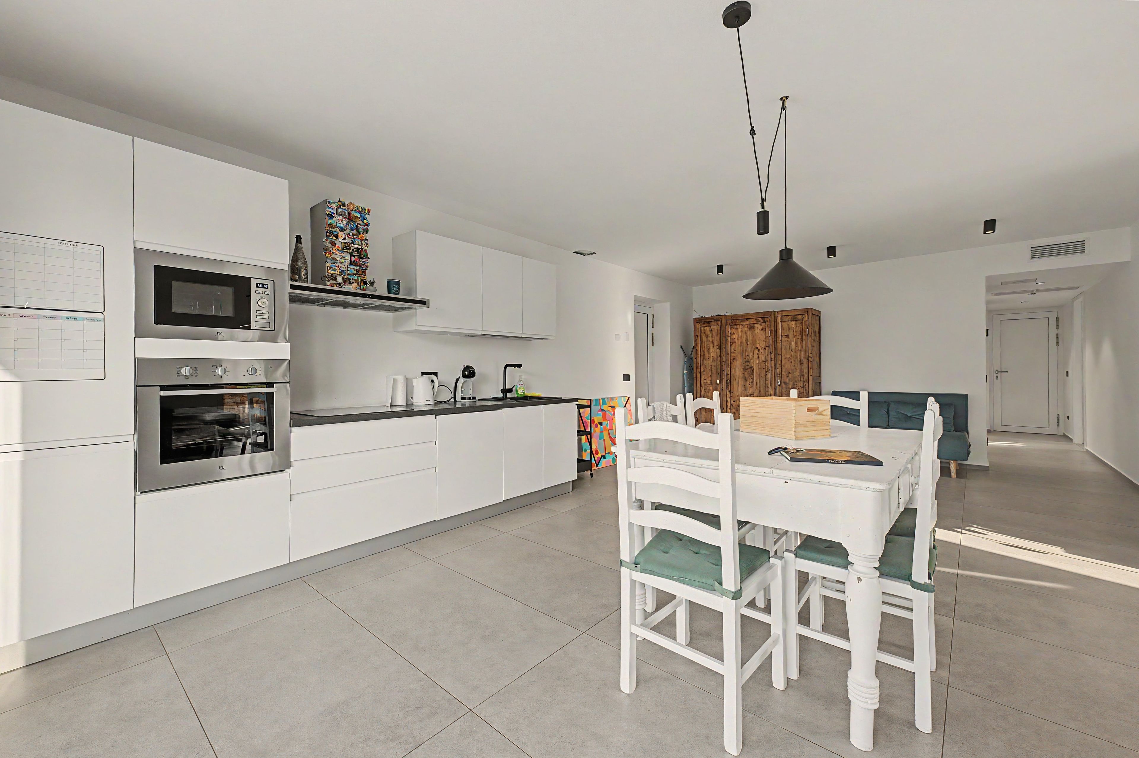 Una cuina moderna amb armaris blancs, forn integrat i zona de menjador amb taula i cadires blanques.