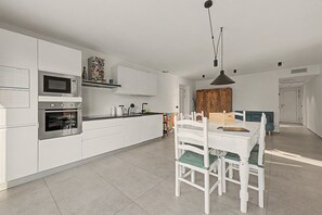 A modern kitchen with white cabinetry, a built-in oven, and a dining area with a white table and chairs.