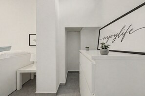 A modern, minimalist bedroom with a bed, bedside table, and a wall-mounted mirror with the phrase 'enjoy life' in cursive.
